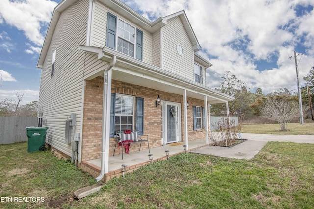 view of front of property featuring a front yard, fence, a porch, and brick siding