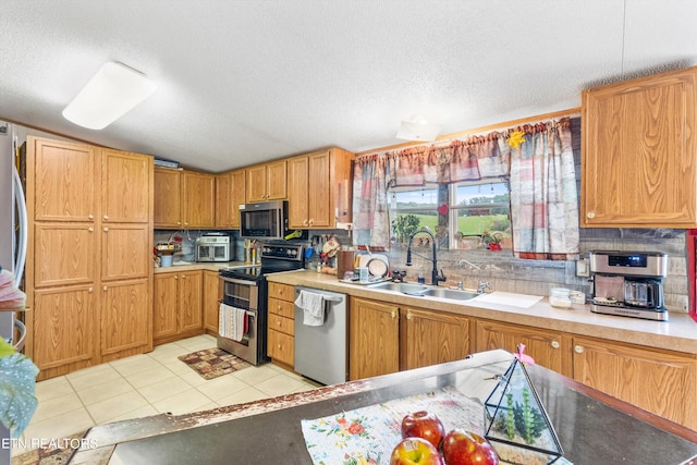 kitchen featuring a textured ceiling, light tile patterned flooring, sink, lofted ceiling, and appliances with stainless steel finishes