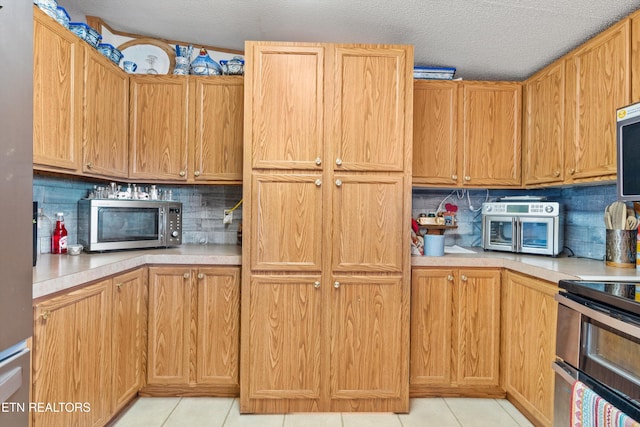 kitchen with appliances with stainless steel finishes, backsplash, a textured ceiling, and light tile patterned floors