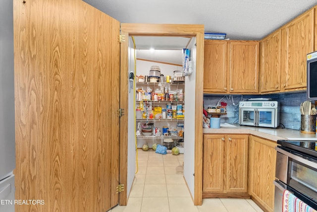 kitchen with appliances with stainless steel finishes, backsplash, a textured ceiling, and light tile patterned floors