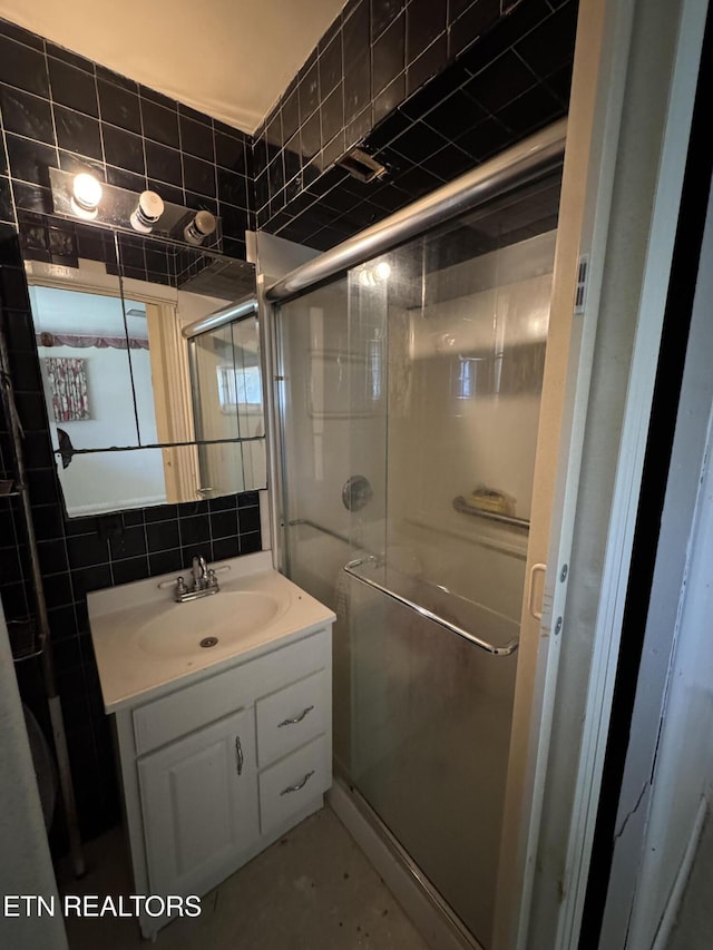 bathroom with a shower with door, vanity, tile walls, and backsplash