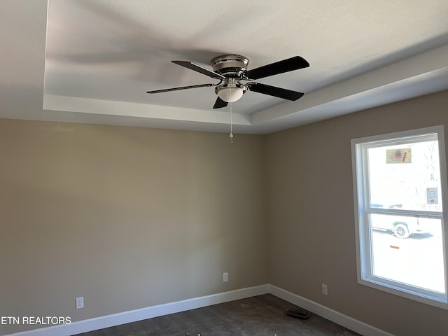 unfurnished room with ceiling fan, baseboards, and a raised ceiling