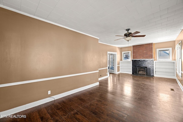 unfurnished living room featuring built in shelves, ceiling fan, crown molding, a fireplace, and hardwood / wood-style flooring