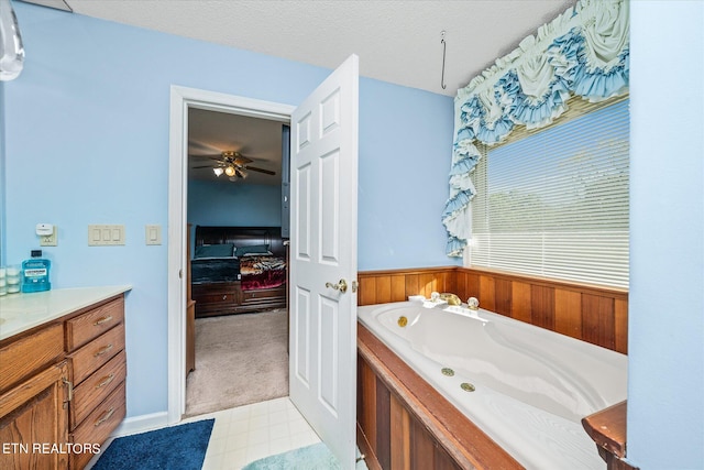 bathroom with a tub to relax in, ceiling fan, wooden walls, vanity, and a textured ceiling