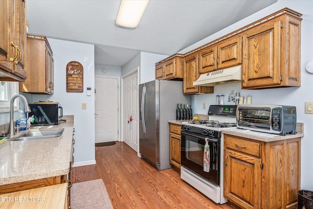 kitchen with a textured ceiling, light wood-type flooring, gas range gas stove, and stainless steel fridge with ice dispenser