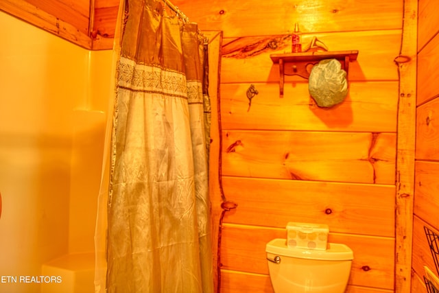 bathroom with wood walls, toilet, and a shower with shower curtain