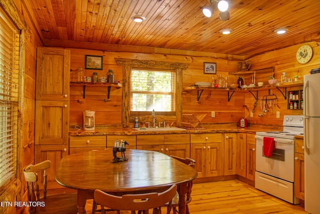 kitchen with wooden walls, white appliances, sink, and light hardwood / wood-style floors