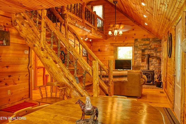 unfurnished dining area featuring wood ceiling, wood walls, a wood stove, high vaulted ceiling, and light wood-type flooring