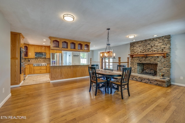 dining room with a chandelier, a stone fireplace, a textured ceiling, and light wood-type flooring