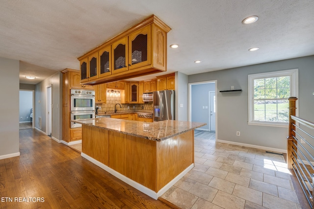 kitchen with decorative backsplash, light stone countertops, light wood-type flooring, sink, and stainless steel appliances