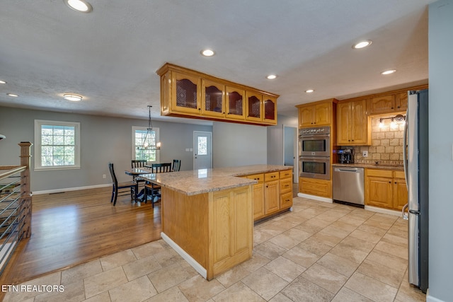 kitchen featuring appliances with stainless steel finishes, backsplash, a center island, light hardwood / wood-style floors, and decorative light fixtures