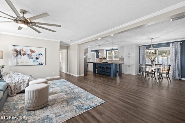 living room with ceiling fan with notable chandelier, a textured ceiling, dark hardwood / wood-style floors, and crown molding