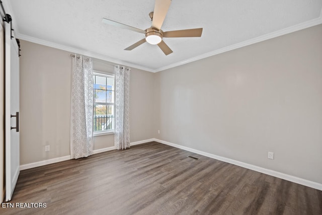 spare room featuring ceiling fan, dark wood-type flooring, crown molding, and a barn door