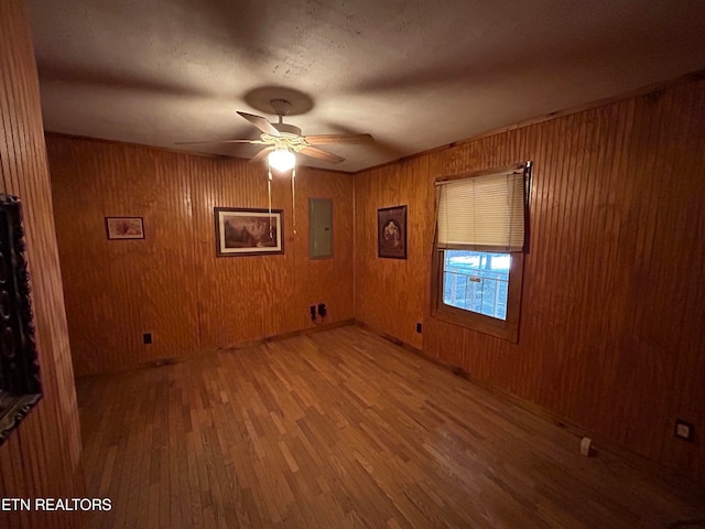 spare room with wood walls, hardwood / wood-style floors, ceiling fan, and electric panel