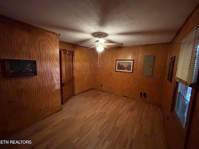 spare room with ceiling fan, electric panel, wooden walls, and light hardwood / wood-style floors