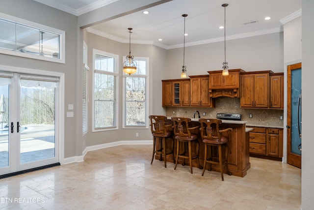 kitchen featuring backsplash, a kitchen island with sink, a breakfast bar area, decorative light fixtures, and ornamental molding