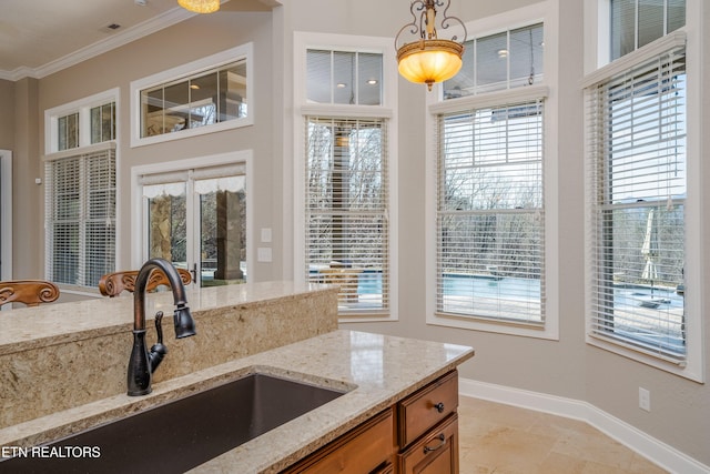 kitchen featuring pendant lighting, light stone counters, crown molding, and sink