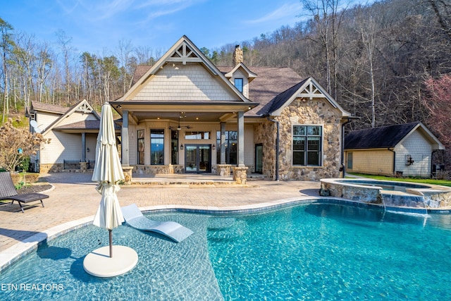 back of property with ceiling fan, a patio area, pool water feature, a pool with hot tub, and an outbuilding