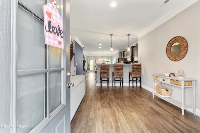 kitchen featuring ornamental molding, kitchen peninsula, wood-type flooring, decorative light fixtures, and a breakfast bar area