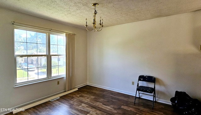 unfurnished room with a textured ceiling, dark hardwood / wood-style floors, and a chandelier