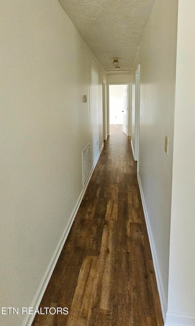 corridor with a textured ceiling and dark hardwood / wood-style flooring