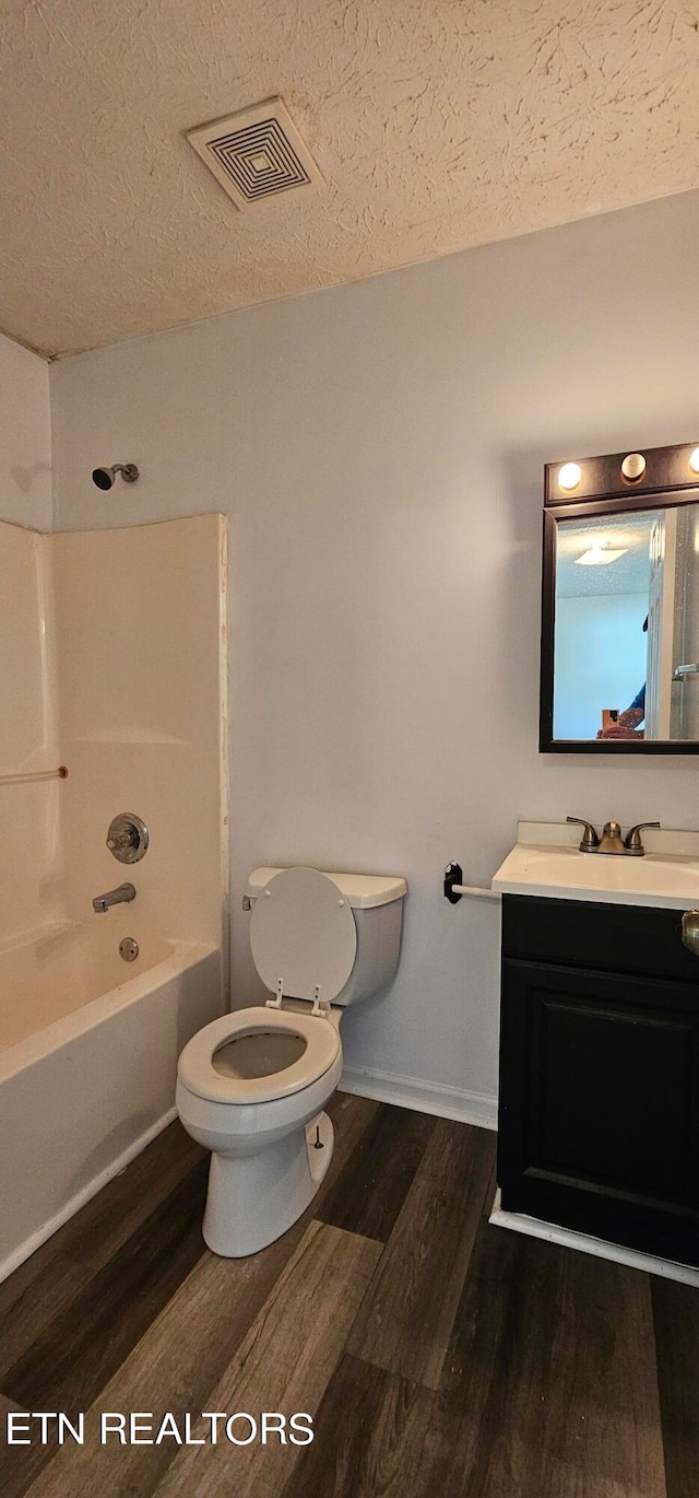 full bathroom featuring a textured ceiling, hardwood / wood-style flooring, tub / shower combination, vanity, and toilet