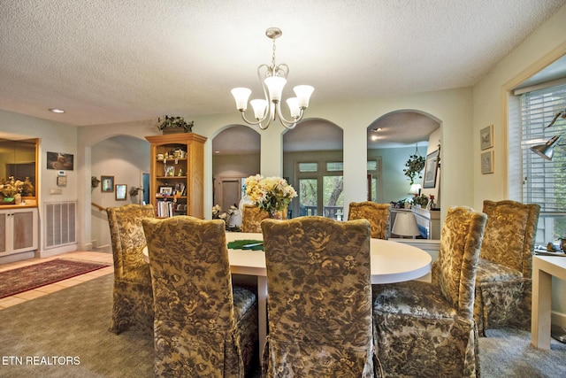 dining room featuring arched walkways, a textured ceiling, a notable chandelier, and carpet