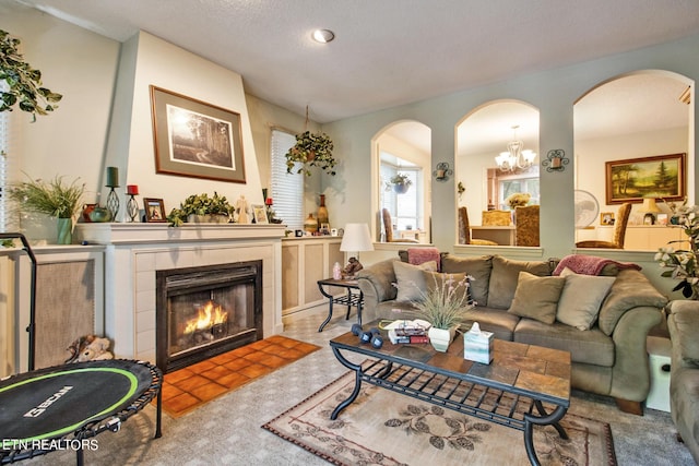 living area featuring a tiled fireplace, arched walkways, an inviting chandelier, and carpet