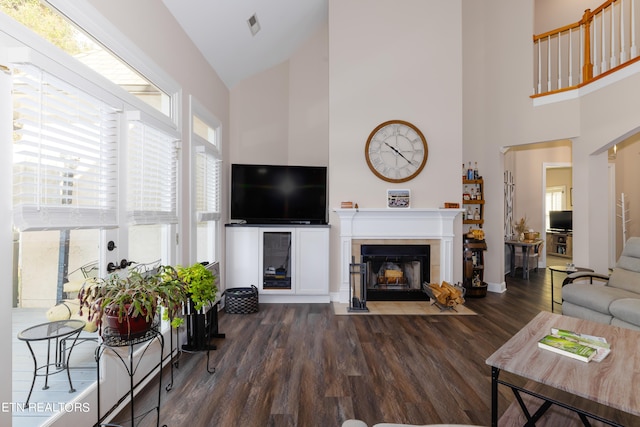 living room with dark wood-type flooring, a tiled fireplace, and high vaulted ceiling