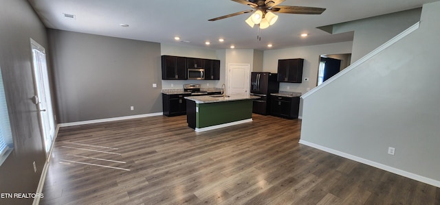 kitchen with a kitchen island with sink, ceiling fan, light stone counters, dark hardwood / wood-style floors, and appliances with stainless steel finishes