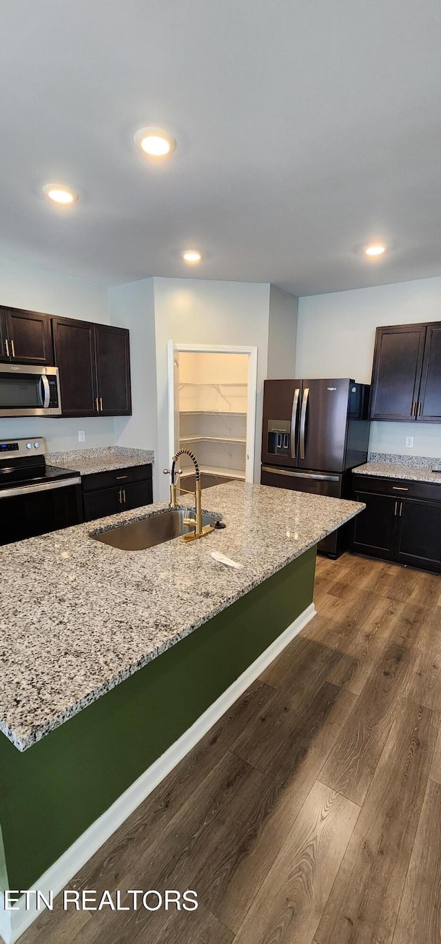 kitchen with dark brown cabinets, light stone counters, stainless steel appliances, and dark hardwood / wood-style flooring