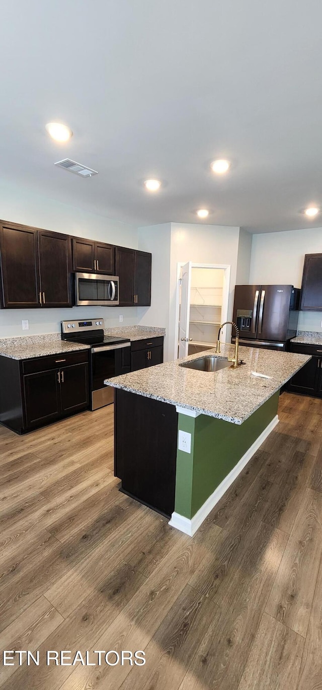 kitchen featuring light hardwood / wood-style floors, a kitchen island with sink, sink, stainless steel appliances, and light stone countertops