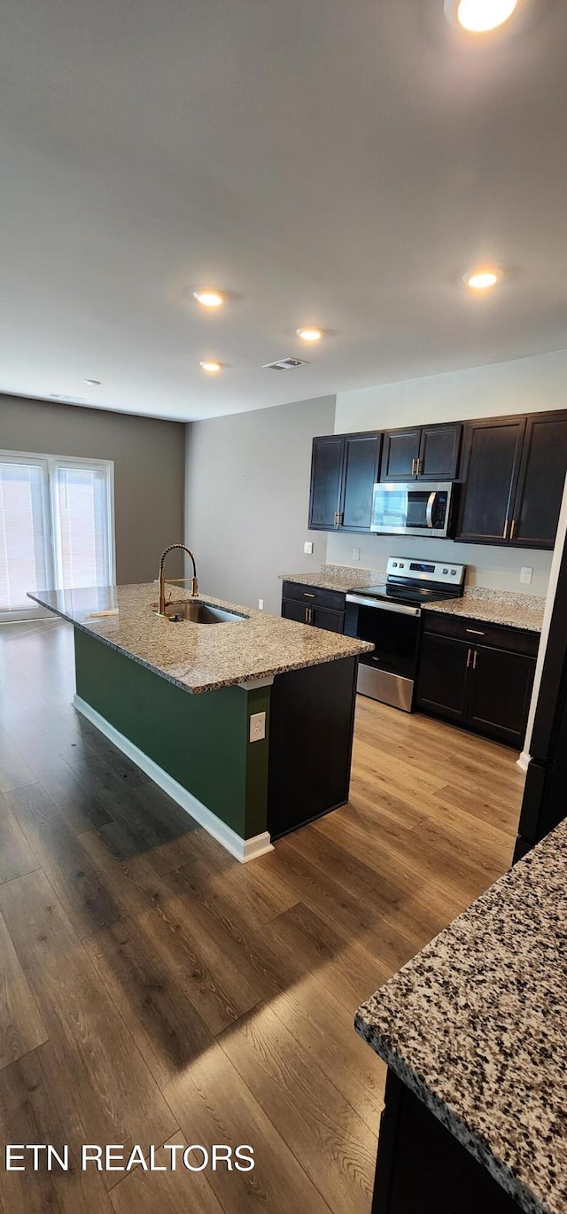 kitchen featuring stainless steel appliances, wood-type flooring, an island with sink, and sink