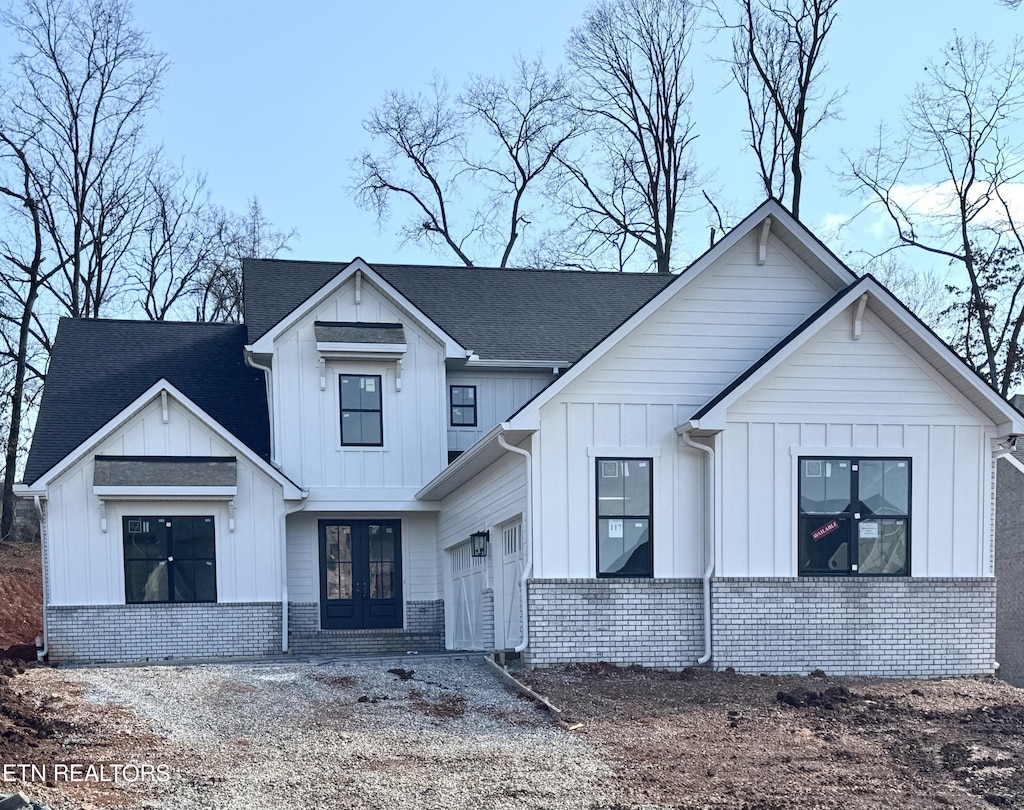 modern farmhouse style home featuring a garage, french doors, board and batten siding, and brick siding