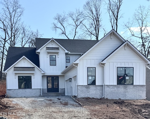 modern farmhouse style home featuring a garage, french doors, board and batten siding, and brick siding