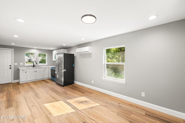 kitchen with stainless steel refrigerator, a wall unit AC, light wood-type flooring, a healthy amount of sunlight, and white cabinetry