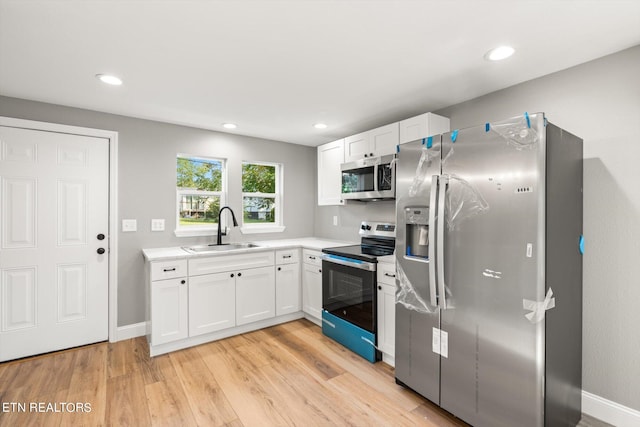 kitchen with light hardwood / wood-style floors, stainless steel appliances, sink, and white cabinetry