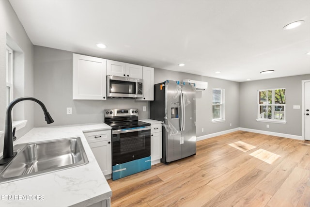 kitchen with light stone counters, sink, white cabinetry, light hardwood / wood-style flooring, and appliances with stainless steel finishes