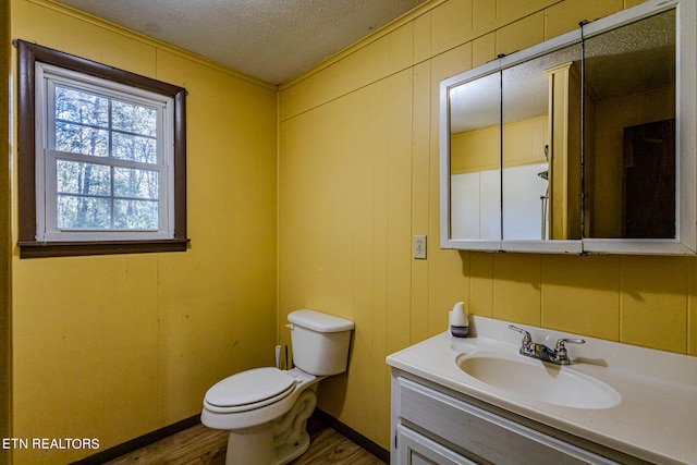 bathroom featuring vanity, wood walls, wood-type flooring, a textured ceiling, and toilet