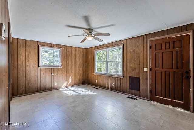 unfurnished room featuring wood walls, plenty of natural light, a textured ceiling, and ceiling fan