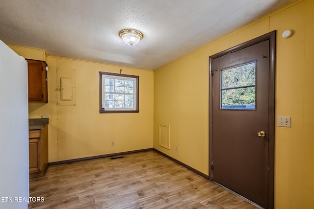 unfurnished dining area with light hardwood / wood-style floors, crown molding, and a textured ceiling