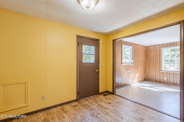 doorway featuring a textured ceiling, light hardwood / wood-style flooring, and wooden walls