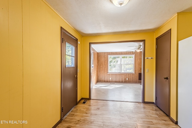 doorway to outside with light wood-type flooring, wooden walls, ceiling fan, and a textured ceiling