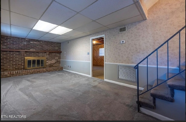 basement with a drop ceiling, a brick fireplace, and carpet floors