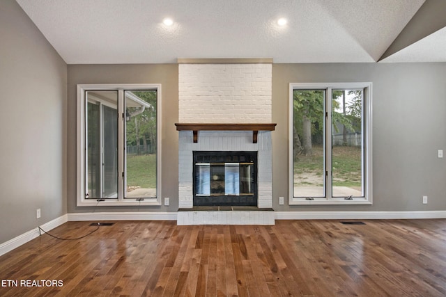 unfurnished living room with a brick fireplace, vaulted ceiling, hardwood / wood-style floors, and a textured ceiling