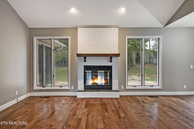 unfurnished living room with a brick fireplace, vaulted ceiling, hardwood / wood-style floors, and a textured ceiling