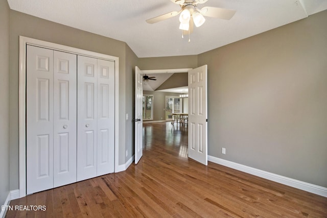 unfurnished bedroom featuring wood-type flooring, a closet, vaulted ceiling, and ceiling fan