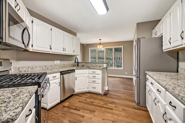 kitchen featuring hardwood / wood-style floors, decorative light fixtures, stainless steel appliances, kitchen peninsula, and white cabinetry