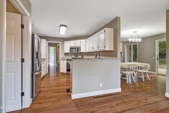 kitchen featuring white cabinetry, dark wood-type flooring, decorative light fixtures, appliances with stainless steel finishes, and a textured ceiling