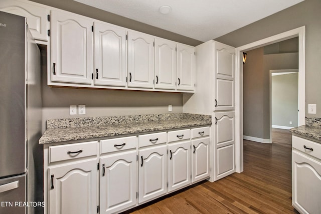 kitchen featuring dark wood-type flooring, stainless steel refrigerator, light stone counters, and white cabinetry